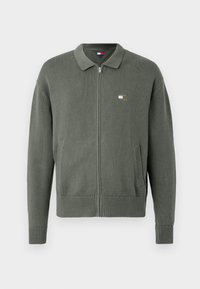Zeleni zip-up kardigan izrađen od teksturiranog pletenog materijala, s ovratnikom, bočnim džepovima i malom logotipom na prsima.