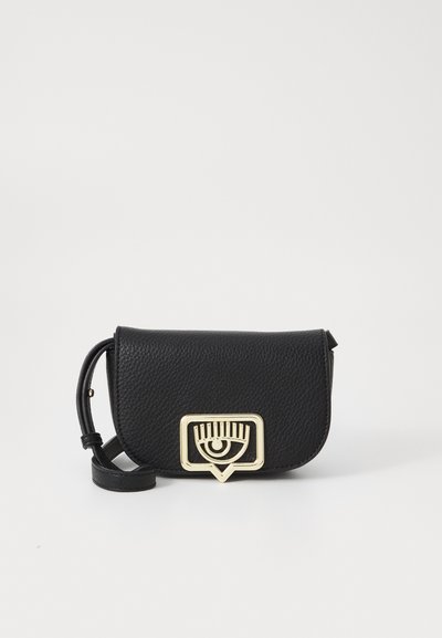 Černá kožená crossbody taška s texturovaným povrchem. Obsahuje zlatý kovový akcent ve tvaru oka a geometrické zapínání.