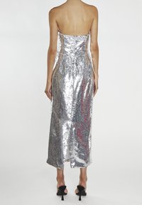 Robe à sequins argentés avec une silhouette droite, un design sans bretelles et une fente dans le dos, dotée d'une doublure intérieure lisse et de talons délicats.