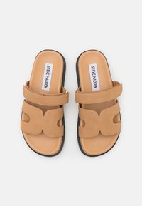 Bruna slide-sandaler med två breda remmar, ett utskuret mönster och en slät ovansida. Texturerad svart sula för grepp. Etikett med texten "STEVE MADDEN."