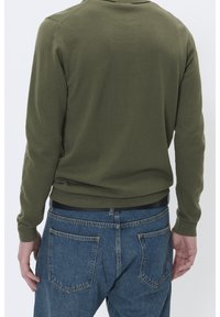 Maglia a maniche lunghe verde oliva con una texture a costine, abbinata a jeans di denim blu con tasche posteriori e cintura nera.