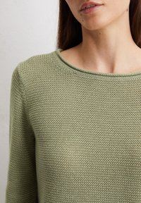 Maglione lavorato a maglia di un verde chiaro, con scollatura rotonda e tessuto testurizzato. Primo piano che mostra il motivo dei punti e la morbidezza della trama.