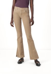 Beige corduroy flared jeans with front pockets, light texture, and split hems, paired with black flat shoes featuring a buckle detail.