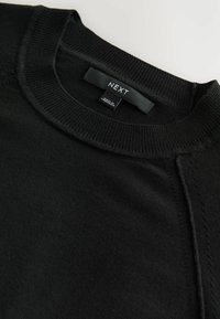 Zwarte sweater met ronde hals en geribbelde kraag en manchetten. Heeft een gladde textuur en een label met de tekst "NEXT" bij de halslijn.