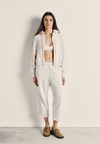 Felpa cropped color crema in pile, pantaloni in pile coordinati e zoccoli in camoscio marrone. Texture morbida, vestibilità casual e design minimalista.