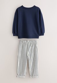 Navyblauwe trui met geribbelde manchetten en halslijn, gecombineerd met wit gestreepte broek met elastische tailleband en omgeslagen pijpen.