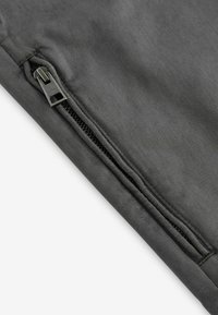 Grauer Stoff mit einer glatten Textur und einem dezenten Reißverschlussdetail. Das Design ist minimalistisch und legt den Fokus auf Funktionalität.