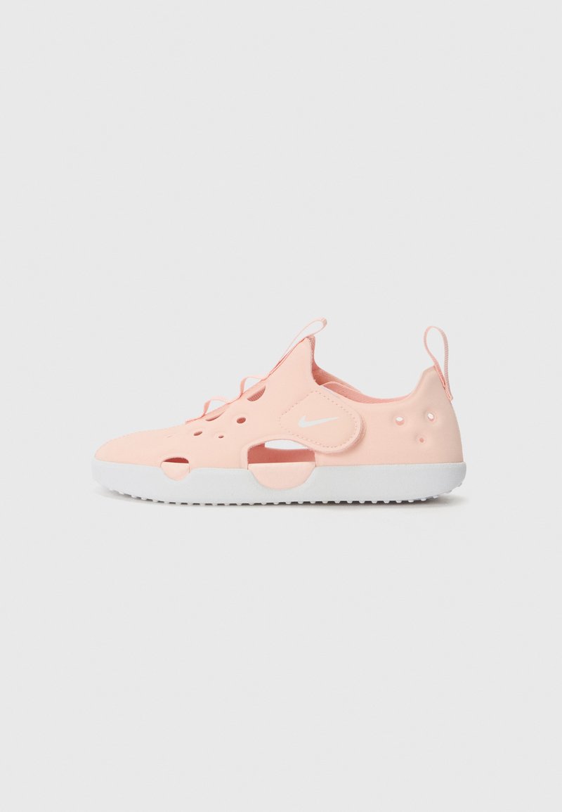 Nike slip-on shoe in soft pink material with cut-out details, white sole, and matching laces. Features a back tab for easy wear.