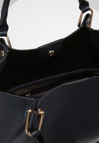 Marinblå läderhandväska med detaljer i guldton, med en texturerad yta, rymligt inre och en dragkedjeficka för säker förvaring.