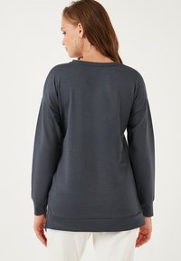 Felpa grigia a maniche lunghe con vestibilità rilassata, scollo rotondo e spacchi laterali all'orlo per comfort e facilità di movimento.