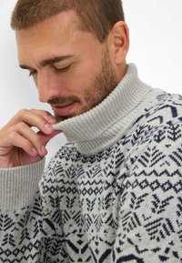 Grauer gestrickter Pullover mit hohem Rippenkragen und dunkelblauen geometrischen Mustern. Verfügt über eine lockere Passform und strukturierte Stoffqualität.