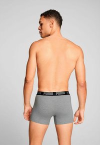 Gray boxer shorts with a black waistband featuring the "PUMA" logo, shown from the back on a model with short hair. Skin visible above the shorts.