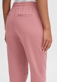 Pink, elastic waistband trousers with a smooth texture; features two back pockets and a relaxed fit, designed for comfort and ease of movement.