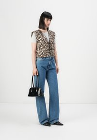 Luipaardprint gilet van zachte stof over een grijze shirt, gecombineerd met hoog opgeslagen blauwe jeans en een kleine zwarte handtas. Puntige schoenen.