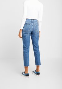 Högmidjade blå denimjeans med rak passform, blekt tvätt, två bakfickor och fransiga anklar, tillsammans med marinblå sneakers.
