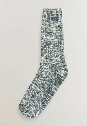 Strikket sok i mørkeblå og hvid meleret mønster, med ribkant og tekstureret stof. Standard crew længde design.