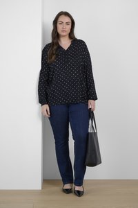 Blouse noire à pois avec des manches longues, décolleté en V ; associée à un jean bleu foncé. Un sac fourre-tout noir et des chaussures noires à talons pointus complètent la tenue.
