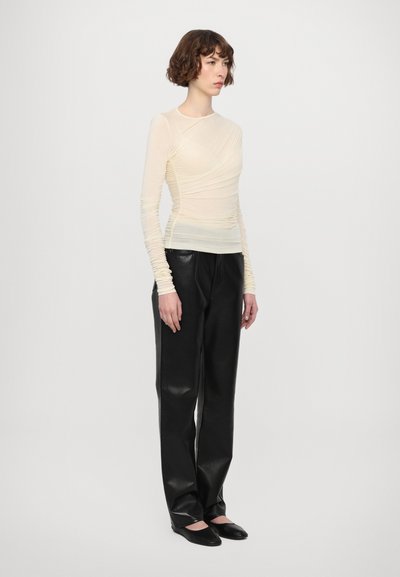 Blusa de manga larga beige claro con textura arrugada, combinada con pantalones de piel negros. El calzado son bailarinas negras. Diseño simple y ajustado.