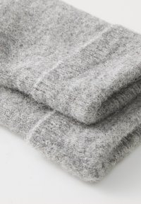 Des chaussettes en laine grises sont pliées, mettant en valeur une texture douce et duveteuse avec un design simple et sans motifs ni accessoires visibles.