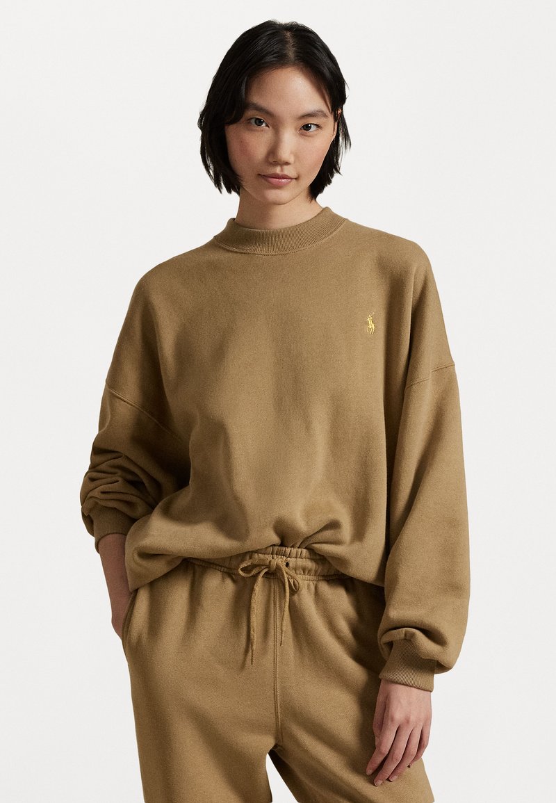 Brown fleece sweatshirt with a high neck, dropped shoulders, and a small yellow logo. Paired with matching drawstring pants. Soft texture.
