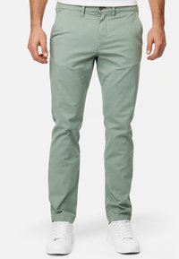 Chinos verde claro de algodón con corte slim; cuentan con bolsillos laterales y cierre de botón. Combinados con zapatillas blancas.