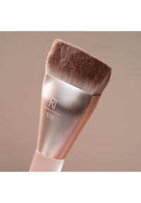 Pinceau de maquillage avec poils bruns denses et inclinés et manche métallique argenté marqué "RT 135" sur fond beige.