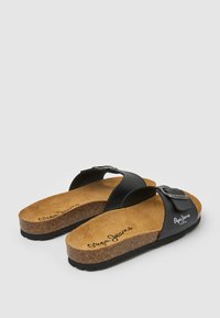 Svarta sandaler med korkfotsäng, med två remmar och spännardetalj. Varumärkeslogotyp tryckt på innersulan. Platt gummisula.