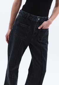 Musta denimhousut rentona, näkyvillä ompeleilla, kahdella takataskulla ja edessä nappikiinnitys. Raskaampi, teksturoitu kangas.