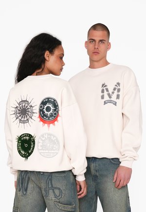 Felpa beige chiaro con stampe grafiche sul retro: design circolari in nero, verde, rosso e bianco. Il davanti mostra un logo.