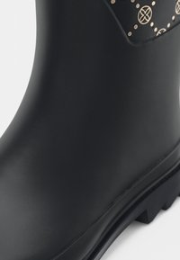 Fekete gumicsizma sima felülettel és díszített mintázattal a tetején. Texturált talp, jól definiált barázdákkal.