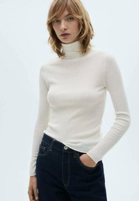 Pull à col roulé blanc côtelé en tissu doux, ajusté et avec des manches longues. Assorti à un jean bleu foncé avec des poches avant.