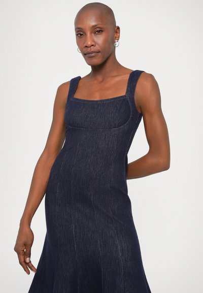 Tmavomodré džínsy šaty s hranatým výstrihom, hrubými ramienkami, priliehavým korzetom a rozšírenou sukňou. Obsahujú viditeľné švy a hladkú textúru.