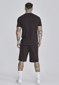 Tamno smeđi pamučni T-shirt i odgovarajuće kratke hlače, kratkih rukava, opuštenog kroja, uparen s bijelim atletskim tenisicama i čarapama do gležnja.