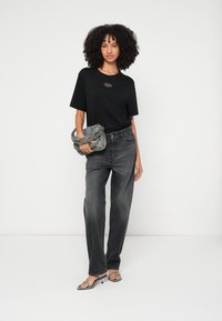 Melna T-krekls ar priekšējā logo, kombinēts ar augsta vidukļa pelēkām džinsām. Modelis nes rakstainu somu un valkā melnas sandales ar siksniņām.