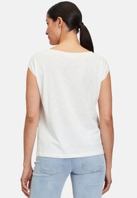 T-shirt blanc à manches courtes avec un large col et un tissu doux, associé à un jean bleu clair présentant un subtil design de poche arrière.