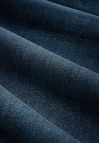 Tmavě modrá denimmová tkanina s texturačním pletením, zobrazuje vlnité záhyby a mírné variace v odstínu a povrchových detailech.