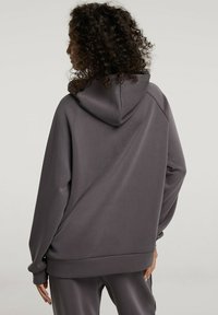 Szara bluza z kapturem wykonana z miękkiego materiału, z dużym kapturem, długimi rękawami oraz luźnym krojem, o gładkiej fakturze i minimalnych detalach.