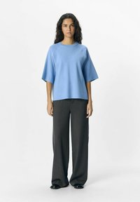 Haut bleu clair à manches courtes, avec une coupe décontractée et des manches raglan, associé à un pantalon large gris foncé et des chaussures noires.
