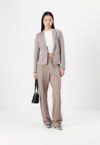 Beige sako na míru s klopami, doplněné kalhotami se šňůrkou ve stejné barvě. Texturovaná tkanina, elegantní kabelka a stříbrné špičaté boty.