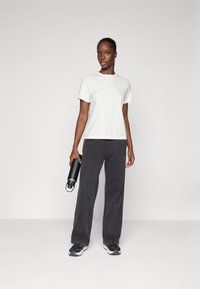 Ανοιχτό γκρι κοντομάνικο μπλουζάκι σε συνδυασμό με σκούρο γκρι παντελόνι φαρδύ. Το μοντέλο κρατάει ένα μαύρο μπουκάλι νερού. Τα αθλητικά παπούτσια είναι μαύρα με λευκές λεπτομέρειες.