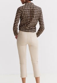 Blusa negra con un patrón geométrico y mangas largas, combinada con pantalones cortos beige con bolsillos traseros y un diseño ajustado.