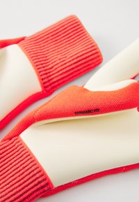 Rode handschoenen met een ribbelgebreide manchette en een gladde latex palm, met het label "DYNAMIC FIT". Het ontwerp benadrukt flexibiliteit en grip.