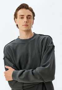 Donkergrijze sweater met een ronde hals, losse pasvorm en versleten details. Beschikt over een zachte textuur en een subtiele, tonale logo-print aan de voorkant.