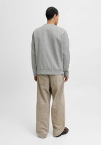 Grå sweatshirt i et enkelt design, parret med beige vide bukser. Skoene har en rund tå og flad sål.
