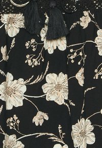 Tessuto nero con stampa floreale in toni beige chiari. Frange nere decorative e pizzo nella parte superiore aggiungono texture e dettagli.