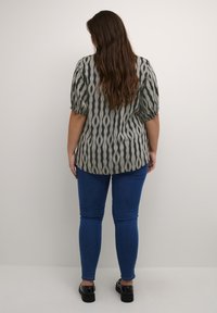 Haut à manches bouffantes en vert olive avec un motif ondulé, associé à un jean skinny bleu et des chaussures à plateforme noires. Tissu texturé avec une coupe décontractée.