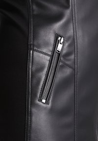 Schwarze Lederjacke mit enganliegender Passform, diagonaler Reißverschlusstasche, glatter Textur und kontrastierenden Nähdetails.