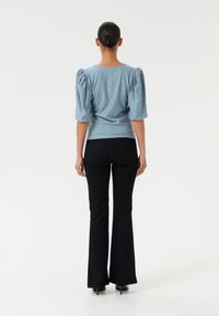 Light blue puff-sleeve top in soft fabric, fitted waist, paired with black flared jeans. Back view highlights sleeve volume and shape.