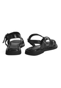 Schwarze Ledersandalen mit mehreren Riemen, einer Schnallenverschlüsse, flacher Gummisohle und einem leicht erhöhten Rand entlang des Fußbettes.