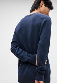 Pulover tricotat de culoare bleu marin, cu textură cordată, guler rotund și mâneci lungi. Spatele prezintă detalii de design subtile și o croială lejeră.